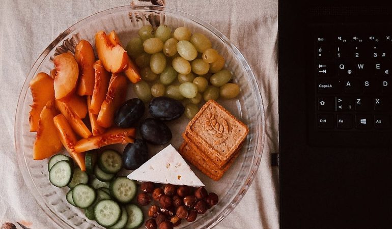 A delightful snack plate with fruits, cheese, and a laptop for a healthy lifestyle.