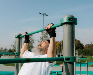 Senior man staying fit with pull-ups in an outdoor park setting, promoting healthy lifestyle.