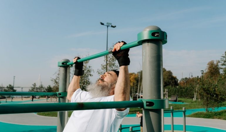 Senior man staying fit with pull-ups in an outdoor park setting, promoting healthy lifestyle.